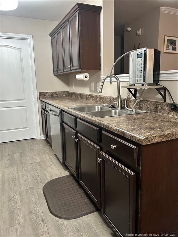 kitchen with dark countertops, dark brown cabinetry, a sink, and light wood finished floors
