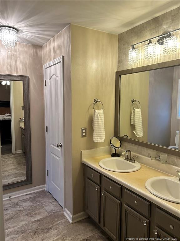 bathroom featuring a sink, baseboards, double vanity, and a chandelier
