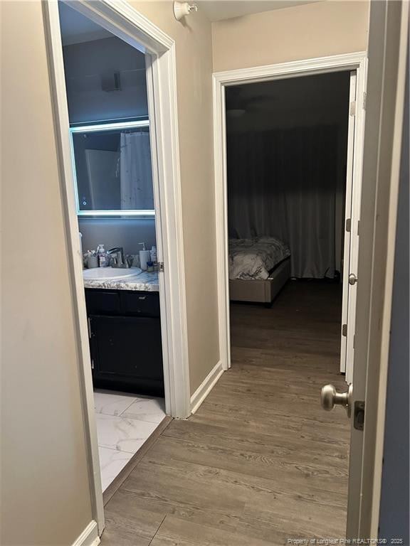 corridor with baseboards, a sink, and wood finished floors