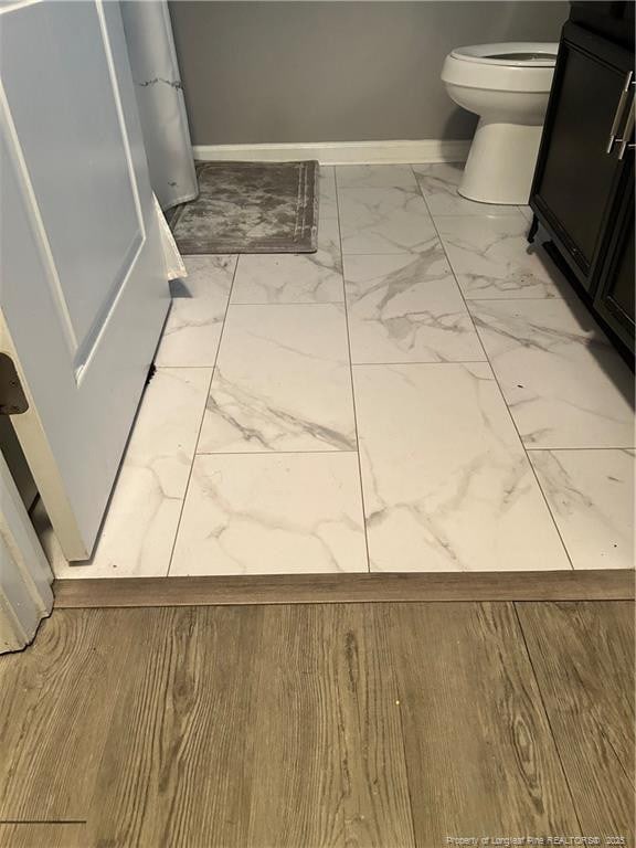 bathroom with toilet, baseboards, and marble finish floor