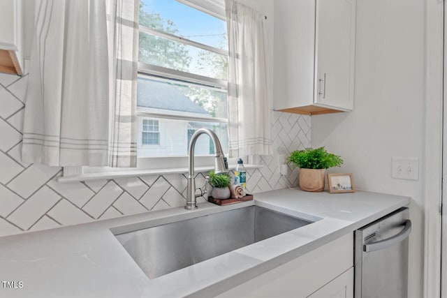 kitchen with stainless steel dishwasher, backsplash, white cabinets, and a sink