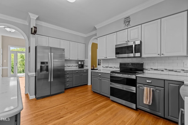 kitchen with appliances with stainless steel finishes, gray cabinets, light wood-style flooring, and arched walkways