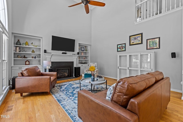 living room with wood finished floors, a towering ceiling, built in features, a ceiling fan, and baseboards