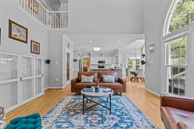 living room with light wood-type flooring, baseboards, a high ceiling, and a notable chandelier