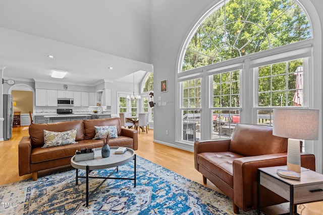 living room featuring baseboards, light wood finished floors, a chandelier, and a high ceiling