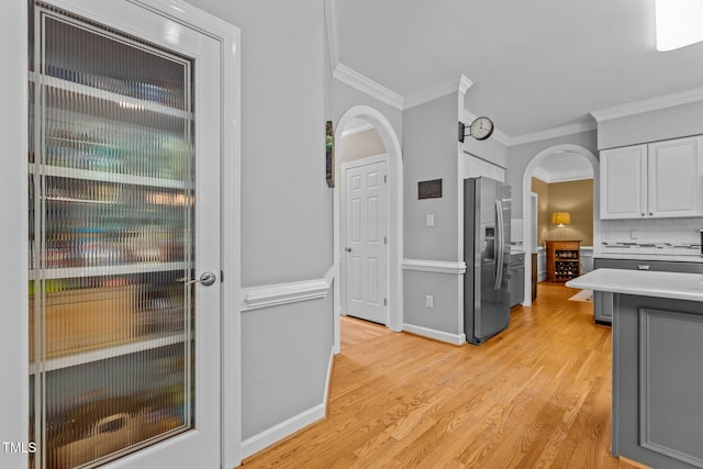 kitchen featuring crown molding, light wood finished floors, white cabinetry, stainless steel fridge, and arched walkways