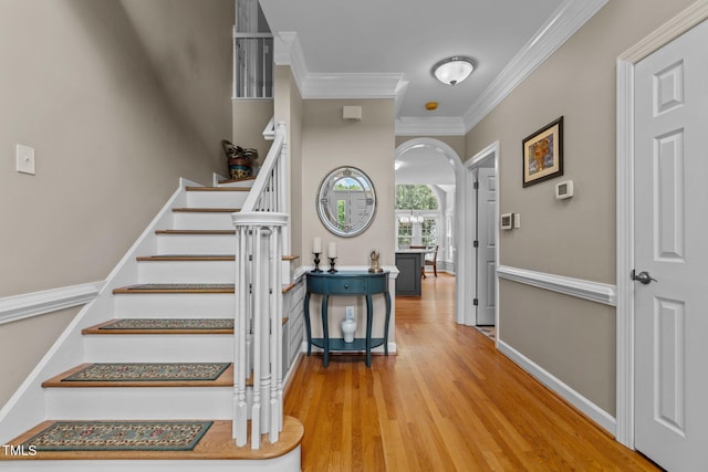 stairs featuring arched walkways, crown molding, and wood finished floors