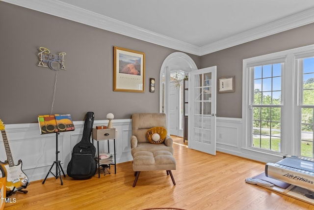 living area featuring french doors, wood finished floors, a decorative wall, wainscoting, and ornamental molding