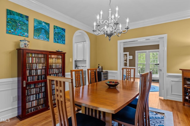 dining area with crown molding, light wood finished floors, an inviting chandelier, arched walkways, and wainscoting