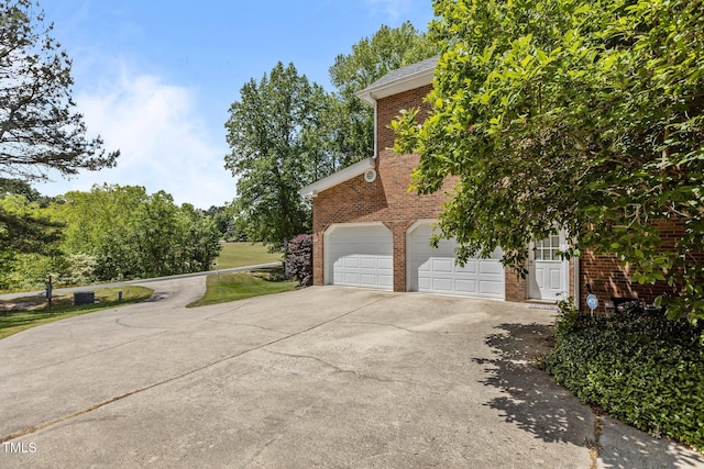 view of side of home featuring driveway, brick siding, and a garage
