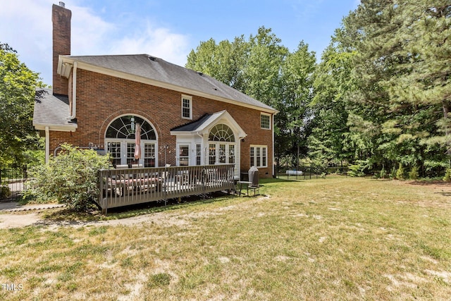 rear view of property featuring a chimney, a lawn, a deck, fence, and brick siding