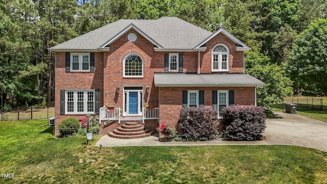 colonial inspired home with fence, a shingled roof, brick siding, and a front yard