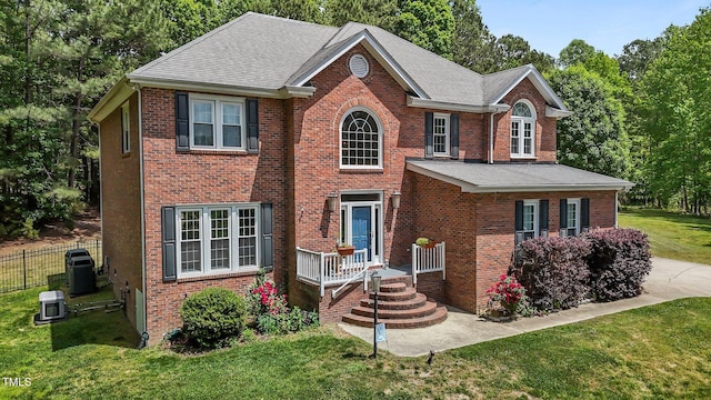 view of front of property with central AC, fence, a front lawn, a shingled roof, and brick siding