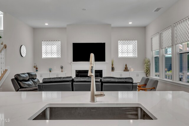 kitchen featuring a fireplace, a sink, light stone counters, open floor plan, and a wealth of natural light