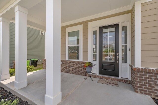 view of exterior entry featuring a porch and brick siding