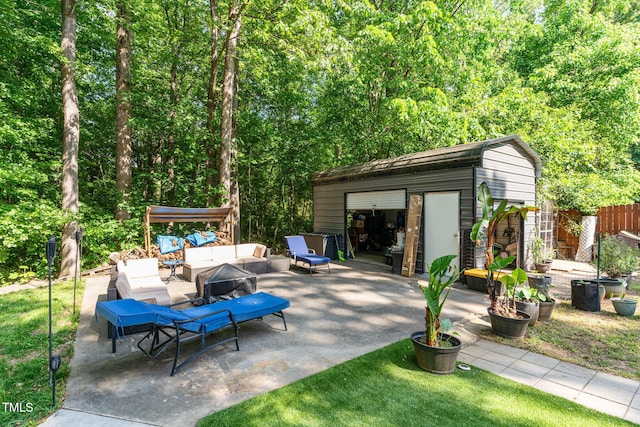 view of patio / terrace with a detached garage, fence, an outbuilding, and an outdoor living space with a fire pit