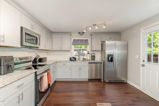 kitchen with dark wood-style flooring, light stone counters, a sink, appliances with stainless steel finishes, and backsplash