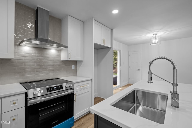 kitchen featuring stainless steel electric range oven, wall chimney range hood, a sink, light wood-style flooring, and white cabinetry
