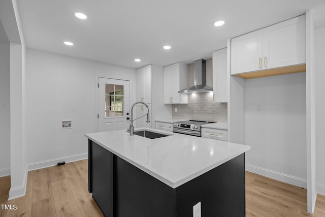 kitchen featuring electric stove, wall chimney range hood, white cabinets, a sink, and light wood-style flooring