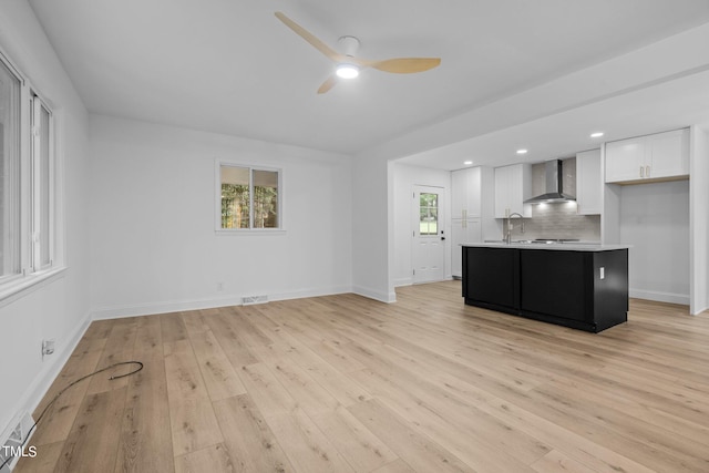 kitchen featuring wall chimney range hood, a ceiling fan, white cabinetry, and light wood-type flooring
