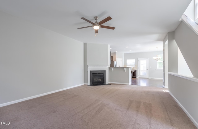 unfurnished living room with carpet floors, ceiling fan with notable chandelier, recessed lighting, baseboards, and a fireplace with flush hearth