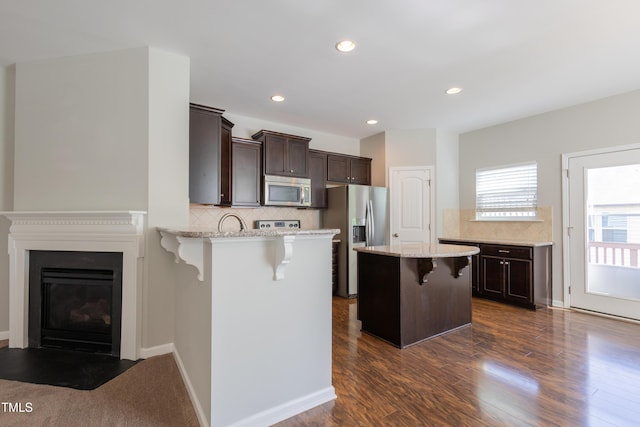kitchen with stainless steel appliances, tasteful backsplash, a kitchen breakfast bar, and dark brown cabinets