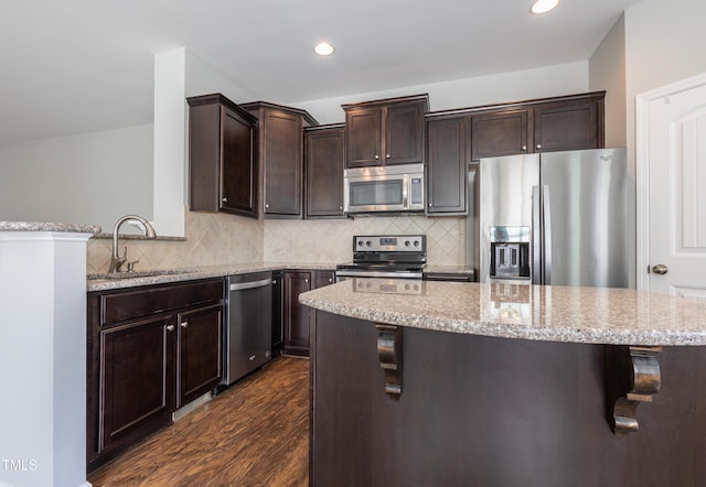 kitchen with stainless steel appliances, light stone countertops, dark wood finished floors, and dark brown cabinets