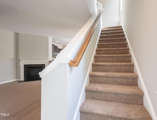 stairs featuring a fireplace with flush hearth, baseboards, carpet flooring, and recessed lighting