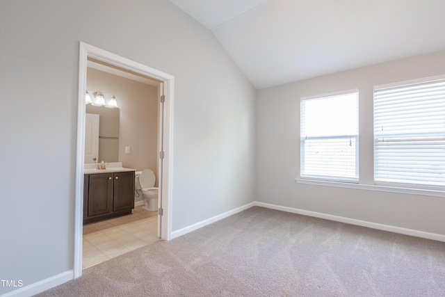 unfurnished bedroom with vaulted ceiling, a sink, baseboards, ensuite bathroom, and light carpet