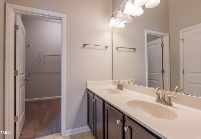 bathroom with baseboards, double vanity, a walk in closet, and a sink