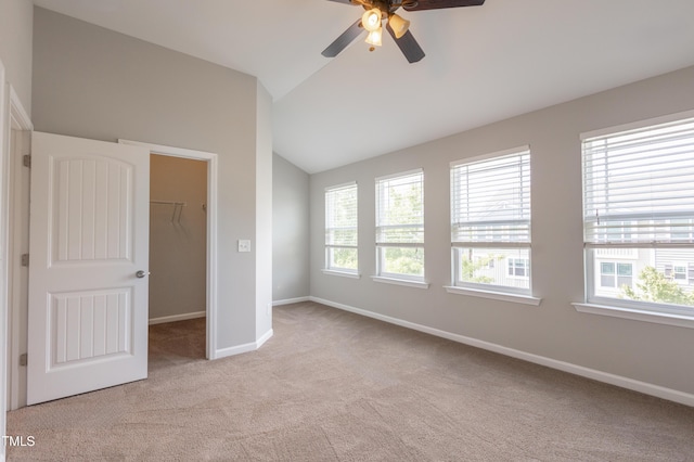 unfurnished bedroom featuring a walk in closet, baseboards, a closet, lofted ceiling, and light carpet