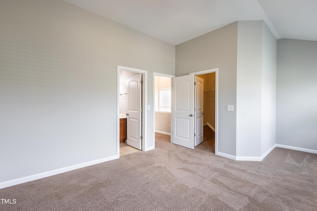 unfurnished bedroom featuring a walk in closet, baseboards, a closet, and light colored carpet