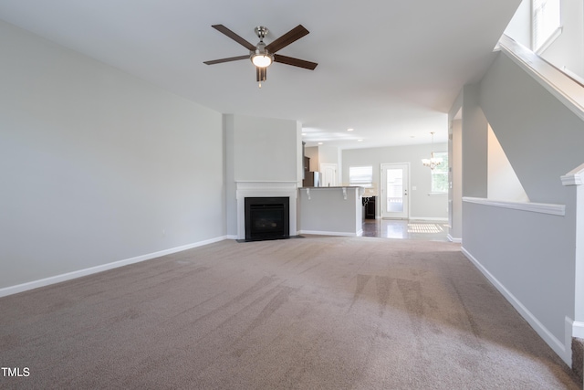 unfurnished living room featuring a fireplace with flush hearth, carpet floors, baseboards, and ceiling fan with notable chandelier