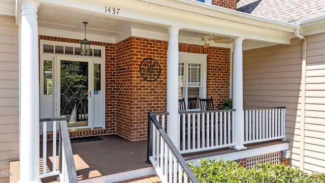 view of exterior entry featuring covered porch, brick siding, and a ceiling fan