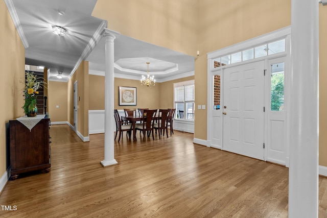 entryway with crown molding, baseboards, a raised ceiling, a chandelier, and light wood finished floors