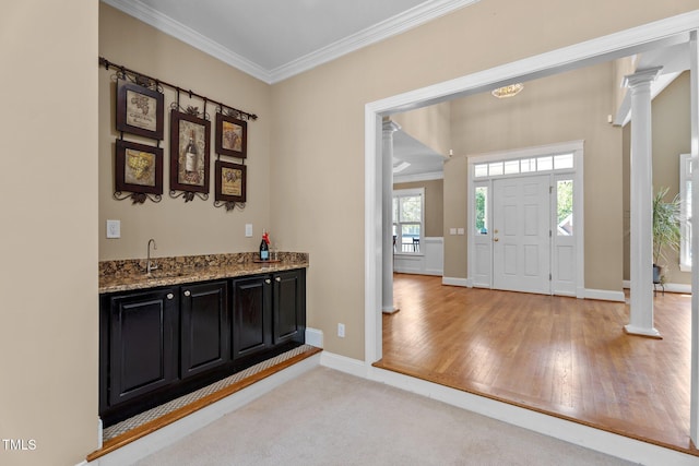foyer entrance with crown molding, ornate columns, wet bar, and baseboards