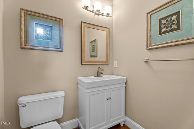 half bath with baseboards, vanity, and toilet
