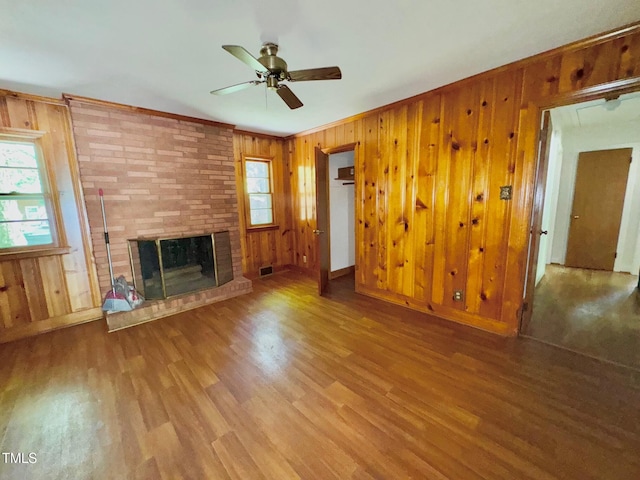 1713 S Garnett St, Henderson, NC 27536 - unfurnished living room featuring wood walls, wood finished floors, a ceiling fan, a brick fireplace, and baseboards