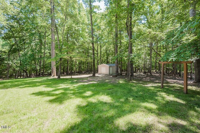 view of green lawn featuring a storage unit, an outbuilding, and a wooded view
