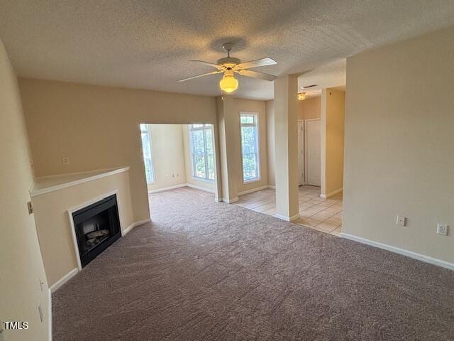 unfurnished living room featuring ceiling fan, light colored carpet, a fireplace, a textured ceiling, and baseboards