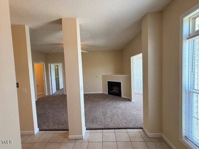 unfurnished living room with a textured ceiling, light colored carpet, a fireplace, light tile patterned floors, and baseboards