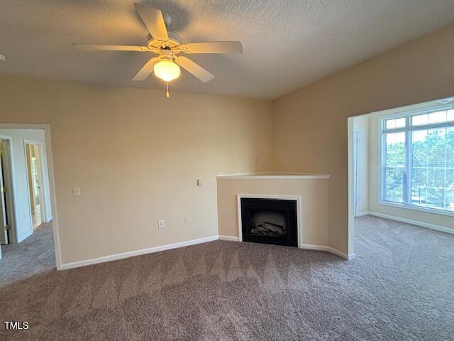unfurnished living room featuring a ceiling fan, a textured ceiling, a fireplace, baseboards, and carpet flooring