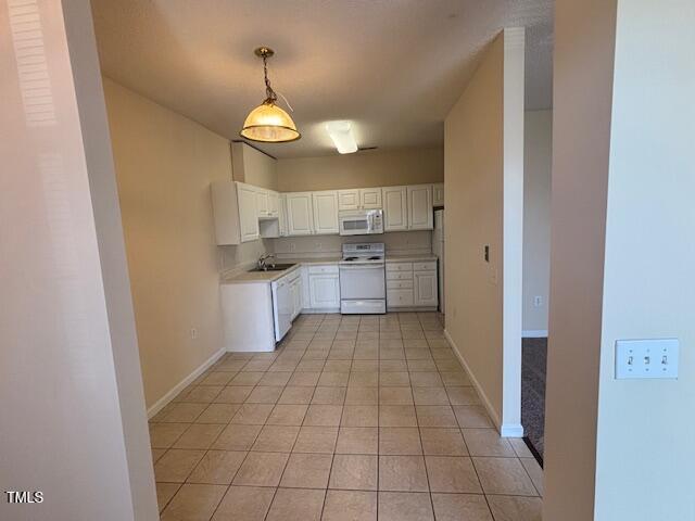 kitchen with light tile patterned flooring, white appliances, light countertops, white cabinetry, and baseboards