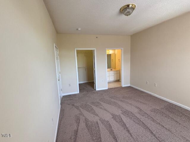 unfurnished bedroom with baseboards, carpet flooring, a textured ceiling, and a spacious closet