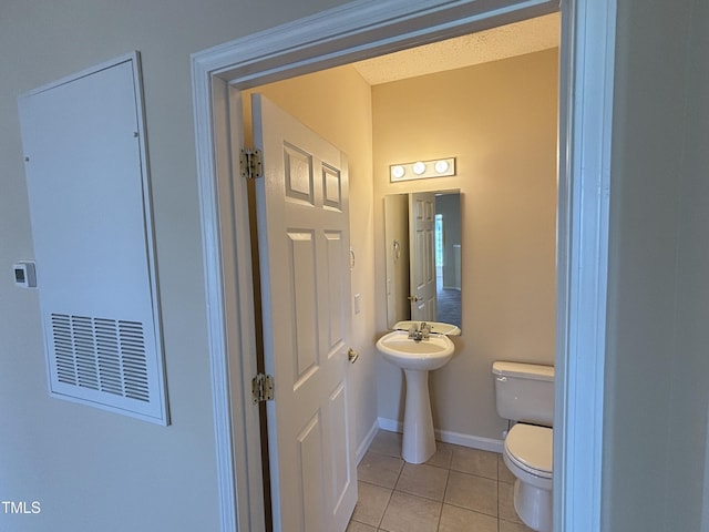 half bath with baseboards, tile patterned floors, and toilet