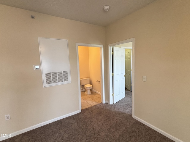 unfurnished bedroom featuring carpet flooring, baseboards, tile patterned floors, and ensuite bathroom