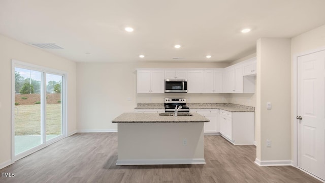 kitchen with appliances with stainless steel finishes, light wood finished floors, light stone counters, and visible vents