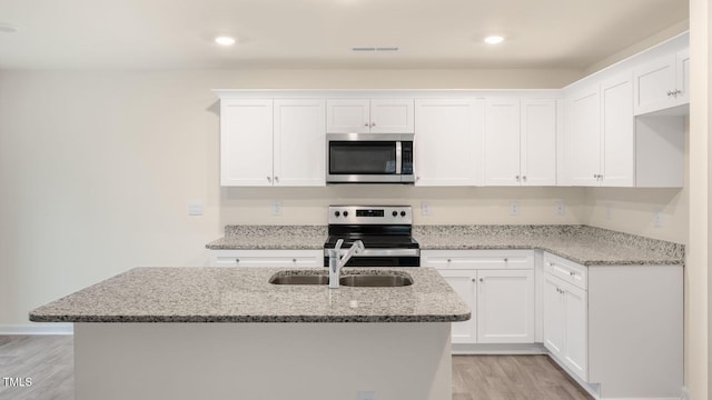 kitchen featuring light stone countertops, appliances with stainless steel finishes, a sink, white cabinetry, and light wood-type flooring