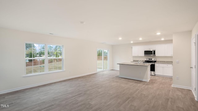 kitchen with appliances with stainless steel finishes, a center island with sink, a sink, light wood-style floors, and recessed lighting