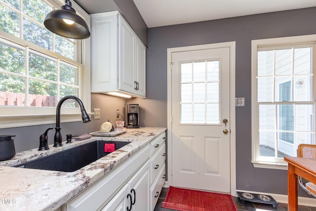 kitchen with baseboards, a sink, white cabinetry, and light stone countertops